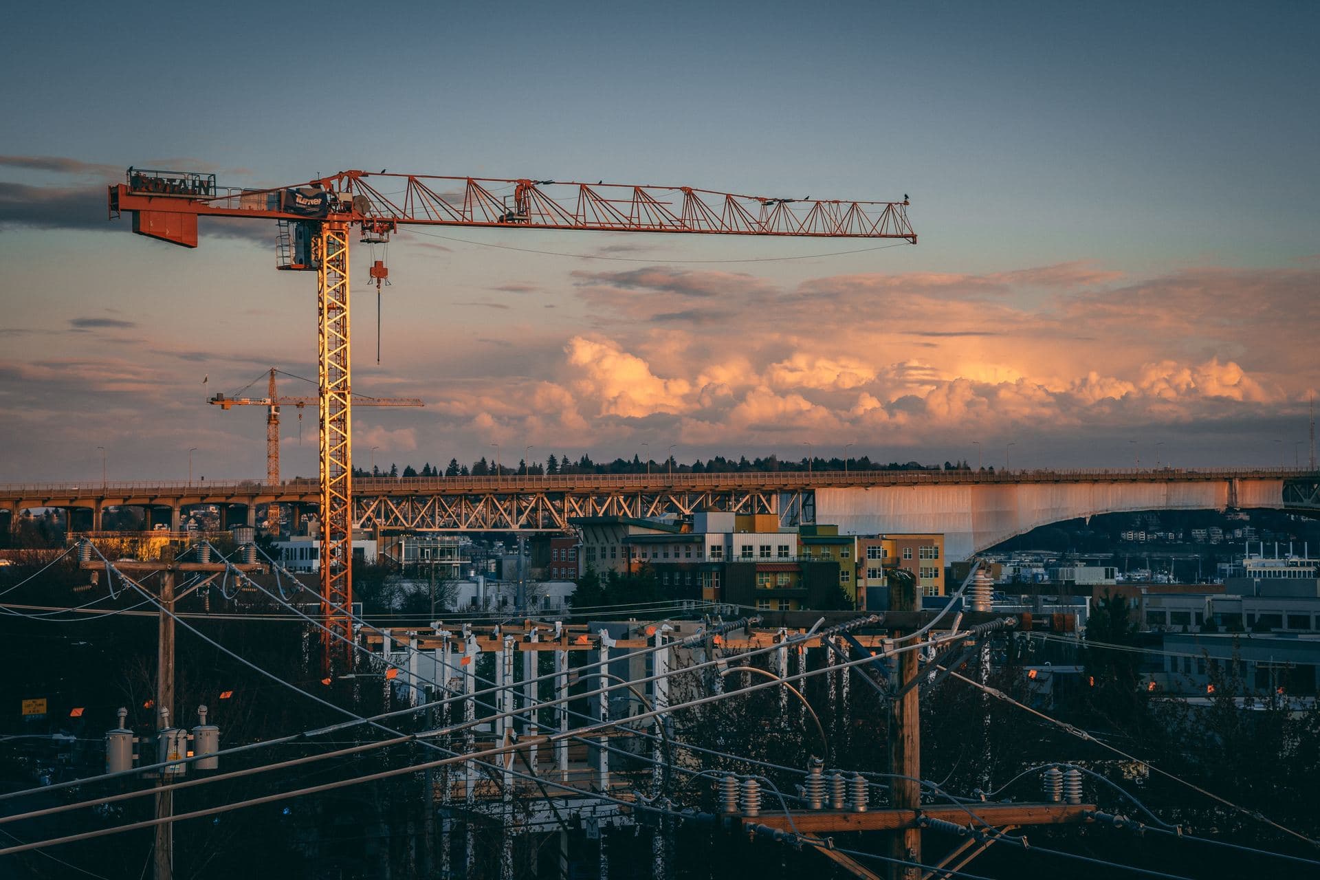 Construction site with tower crane silhouetted against a city skyline at sunset